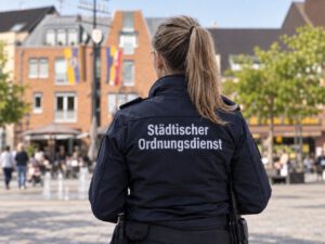KI-generiertes Symbolfoto: Mitarbeiterin des Städtischen Ordnungsdienstes von hinten auf dem Marktplatz in Alt-Willich